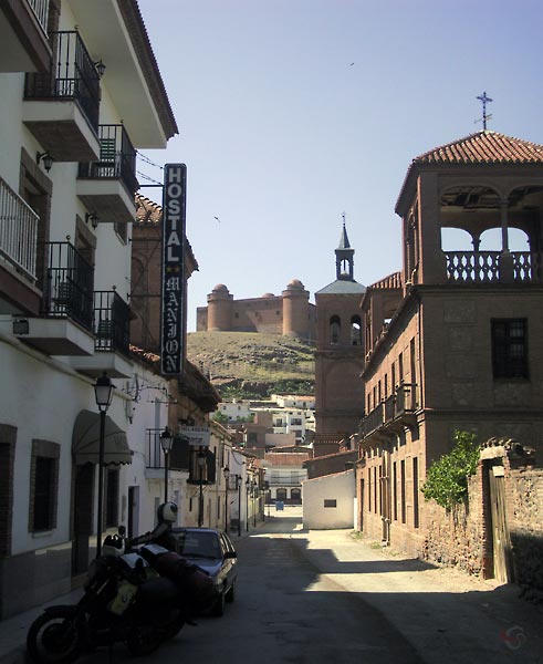 Narrow street with hotel and motorcycle, and a castle in the distance