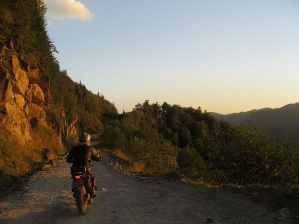 Tricker on unpaved road, light of a setting sun against a rock