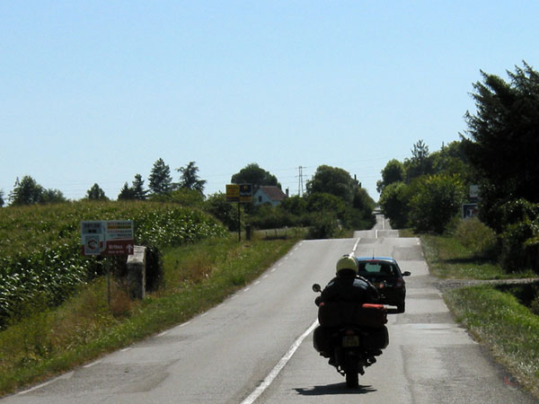 Motorcycle rider behind a car on a road with dips