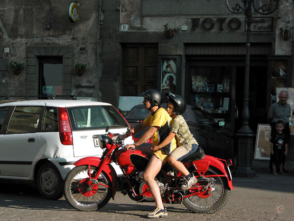 Father and son on an antique motorcycle; both dressed in shorts and T-shirt